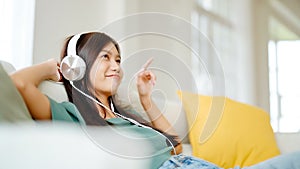 Young asian woman listening to music on couch in living room at home