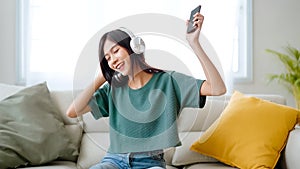 Young asian woman listening to music on couch in living room at home