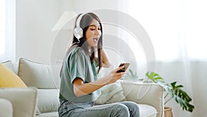 Young asian woman listening to music on couch in living room at home