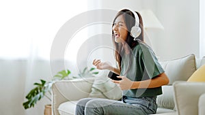 Young asian woman listening to music on couch in living room at home