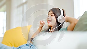 Young asian woman listening to music on couch in living room at home