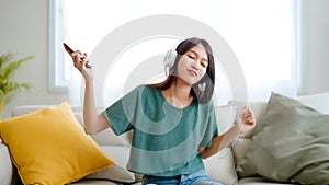 Young asian woman listening to music on couch in living room at home