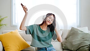 Young asian woman listening to music on couch in living room at home