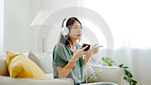 Young asian woman listening to music on couch in living room at home