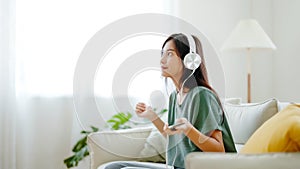 Young asian woman listening to music on couch in living room at home