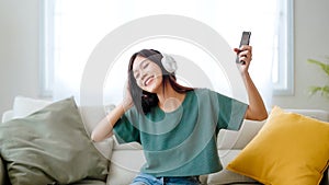 Young asian woman listening to music on couch in living room at home