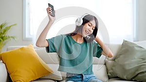 Young asian woman listening to music on couch in living room at home