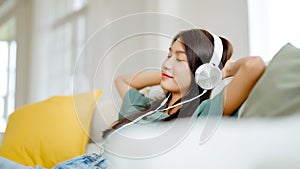 Young asian woman listening to music on couch in living room at home