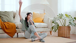 Young asian woman listening to music on on the floor beside couch in living room at home