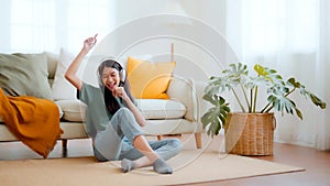 Young asian woman listening to music on on the floor beside couch in living room at home