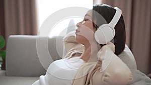 Young asian woman listening to music with headphone and relaxing while sitting on the sofa at home