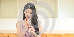 Young Asian woman is listening to music and holding an apple in her hand while standing in the living room