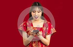 Young asian woman long hairstyle in red dress using smartphone to shopping online, chating and text message on red background