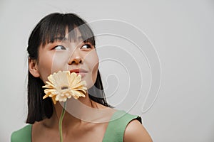 Young asian woman looking aside while posing with gerbera flower