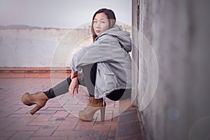 Young Asian woman is looking into the camera while leaning against a wall