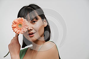 Young asian woman looking at camera while posing with gerbera flower