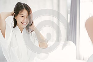 Young Asian woman looking her face in mirror in bathroom.