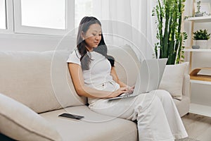 Young Asian woman looking at laptop screen on her lap sitting on couch at home lifestyle work as a freelancer