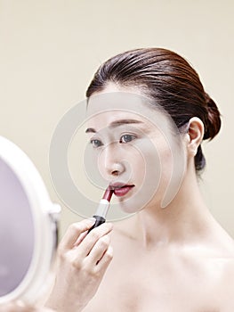 Young asian woman looking in the mirror while applying lipstick