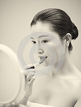 Young asian woman looking in the mirror while applying lipstick
