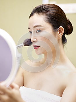 Young asian woman looking in the mirror while applying make-up