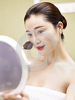 Young asian woman looking in the mirror while applying make-up