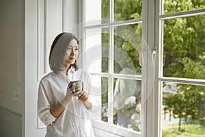 Young asian woman looking out of window at home