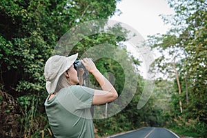 Young asian woman looks through binoculars between a travel.