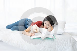 A young Asian woman lounging with a maltese dog on a white bed