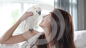 Young Asian woman lying on bed woke up and greeted by a cockatoo parrot in the morning photo