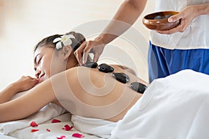 Beautiful Asian woman lying down on massage bed with traditional hot stones along the spine in spa salon, enjoying and relaxing