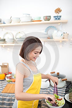 Young asian woman making salad in kitchen smiling and laughing h