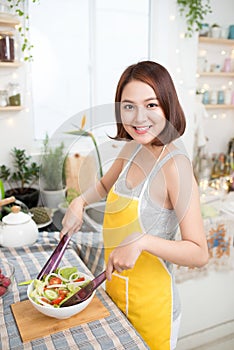 Young asian woman making salad in kitchen smiling and laughing h