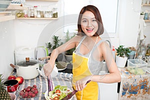 Young asian woman making salad in kitchen smiling and laughing happy at home