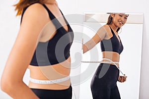 Young Asian woman measuring waist with tape in front of a mirror
