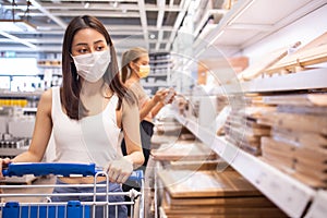 Young asian woman with medical mask looking and shopping in the warehouse store during coronavirus covid-19 pandemic. .After