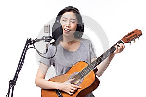 Young asian woman with microphone recording song and playing guitar in music studio, Woman performing in a recording studio for