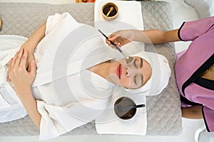 Young asian woman with nutrient facial dressed in bathrobe, getting facial care by beautician at spa salon, Top View. Face peeling