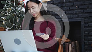 Young asian woman online shopping in Christmas with credit card on laptop computer, female buying and payment.
