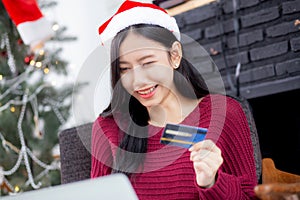Young asian woman online shopping in Christmas with credit card on laptop computer, female buying and payment with debit card.