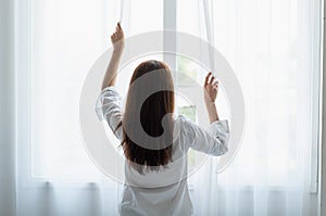 Young Asian woman opening the curtain in the morning after wake up