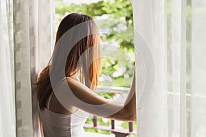 Young asian woman opening curtains in the morning