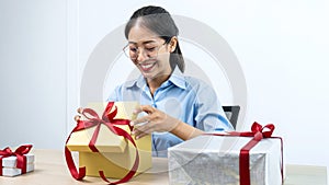 Young asian woman opening a gift box with red ribbon and looking inside box