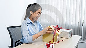 Young asian woman opening a gift box with red ribbon and looking inside box