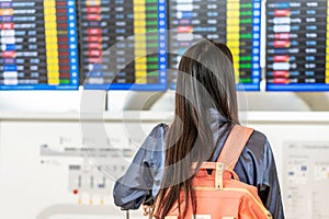 Young asian woman with passport and boarding pass as a hand stand in front of the airline time schedule board looking at the