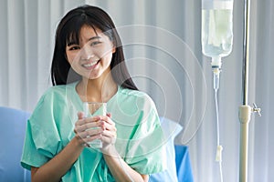 Young asian woman patient smiling as she getting better from her illness. She is holding a glass of pure water with feeling