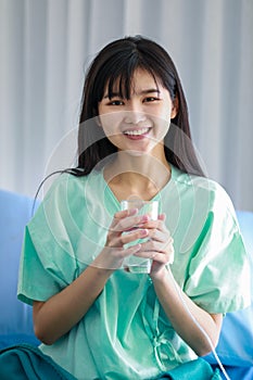 Young asian woman patient smiling as she getting better from her illness. She is holding a glass of pure water with feeling