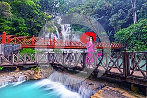 Young Asian woman in pink dress walking on wooden path in Kuang Si waterfall the most popular tourist attractions Lungprabang