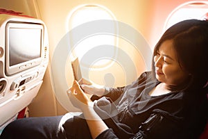 Young asian woman on  plane with smartphone in her hands..Play cell phone on board in airplane near window seat
