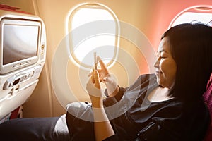 Young asian woman on  plane with smartphone in her hands..Play cellphone on board in airplane near window seat